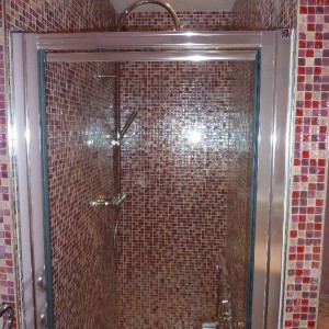 Double shower enclosure tiled in pink glass mosaics with shower screen in place.