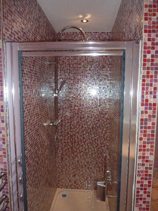 Double shower enclosure tiled in pink glass mosaics with shower screen in place.